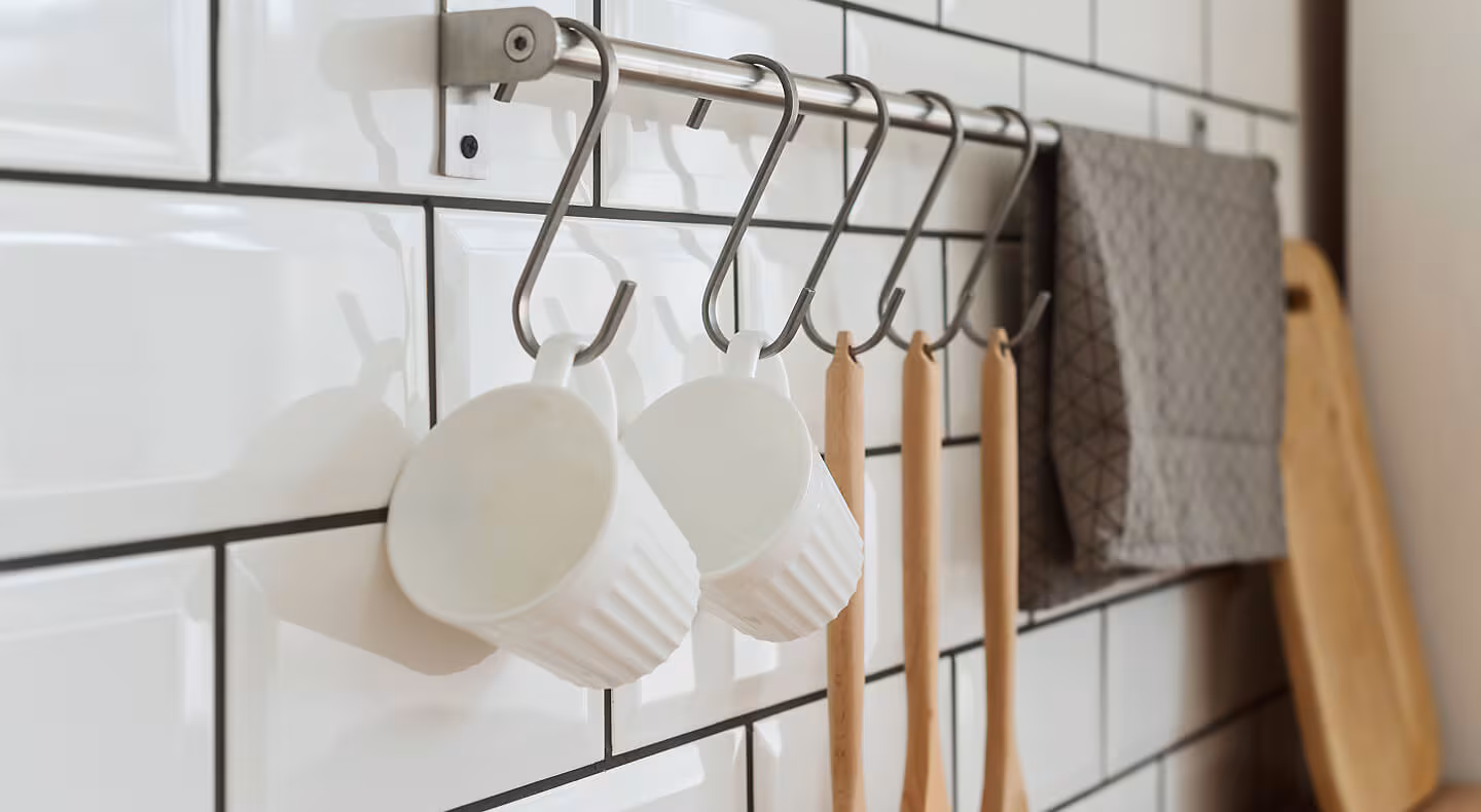 Mugs and wooden mixing spoons hanging from hooks on a rod