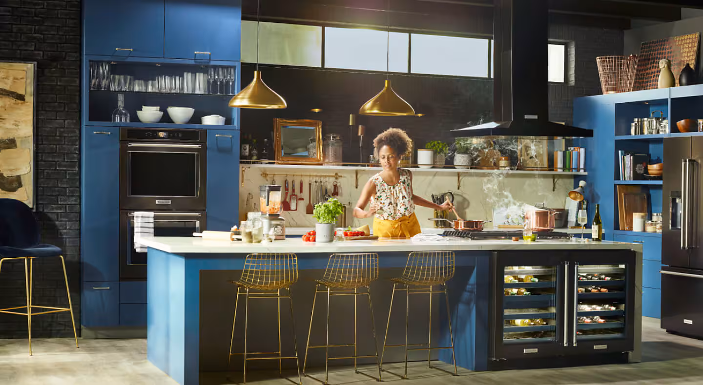 Person cooking in a kitchen with deep blue cabinets and black stainless steel KitchenAid® appliances